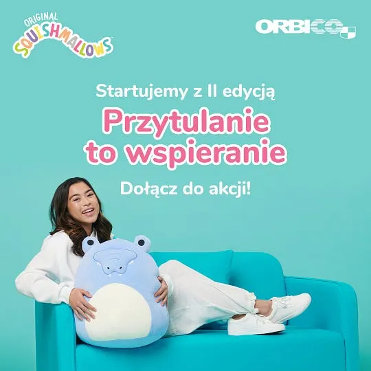Kampania Przytulanie to wspieranie: dziewczyna na turkusowej sofie obejmująca dużą pluszową maskotkę Squishmallows