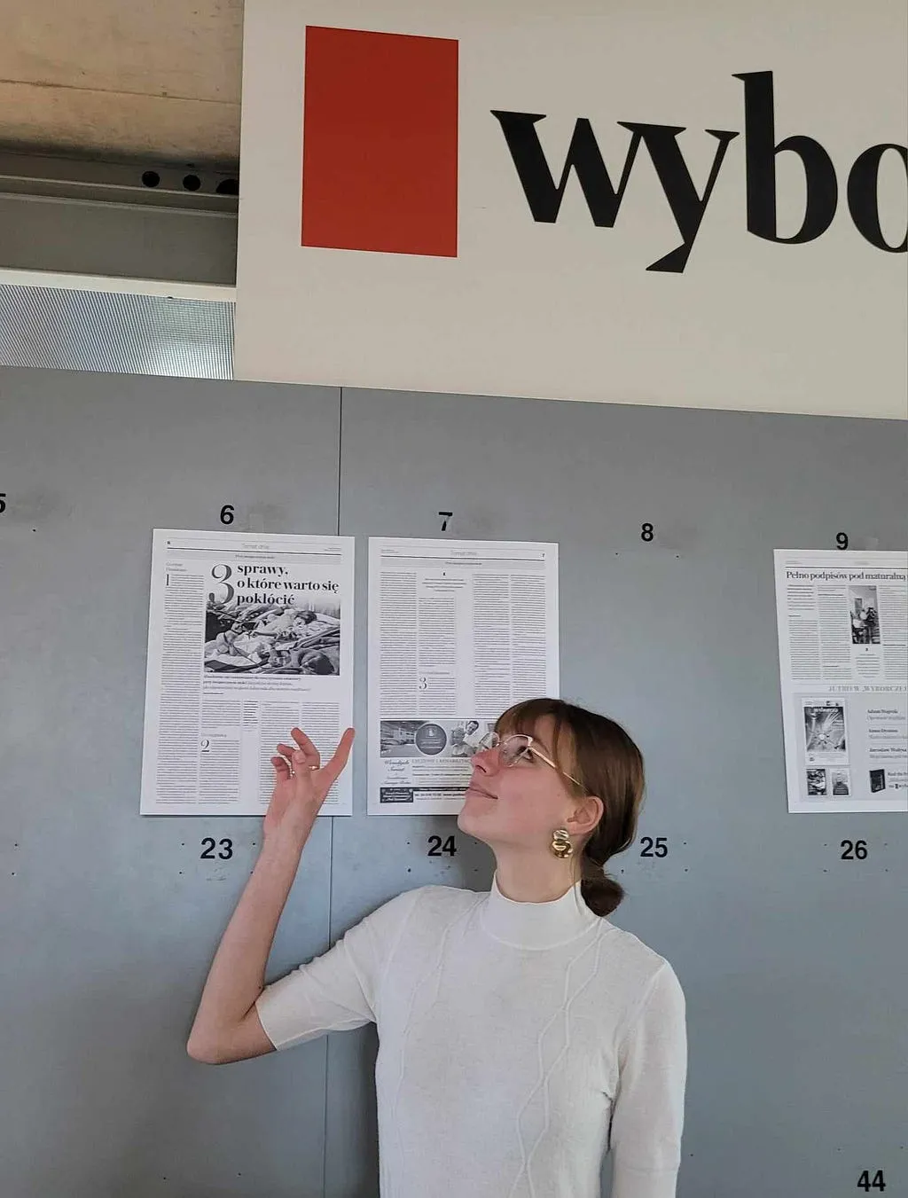 Kalina pointing up at her own article, pinned with the day’s pages on the Wyborcza newsroom wall