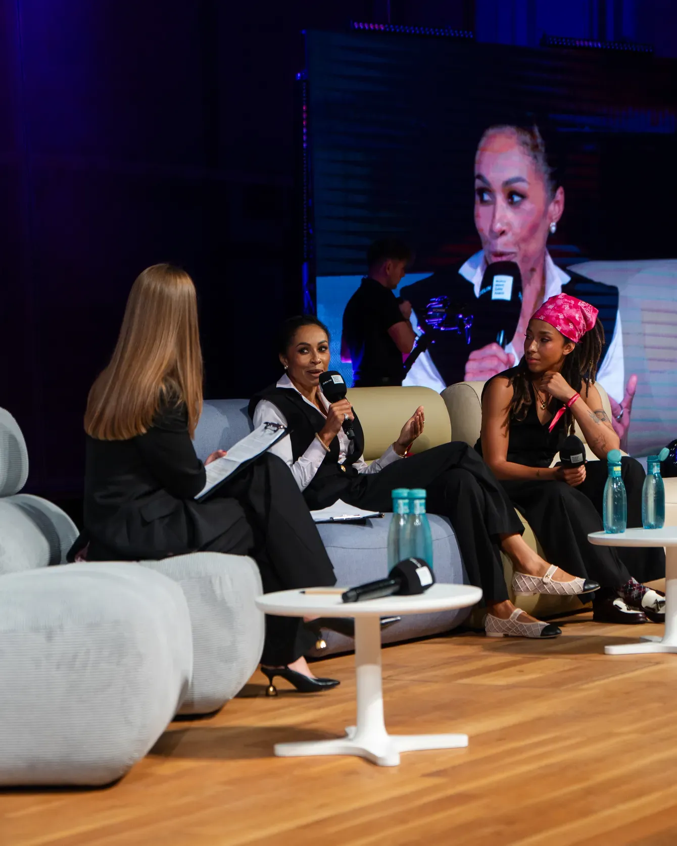 A panel in progress on the Summit stage, three speakers in conversation on the sofas