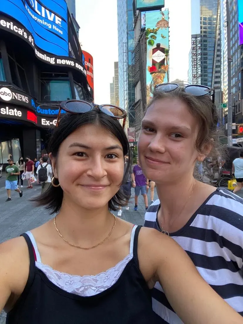Two participants smiling side by side in Times Square, its billboards behind them