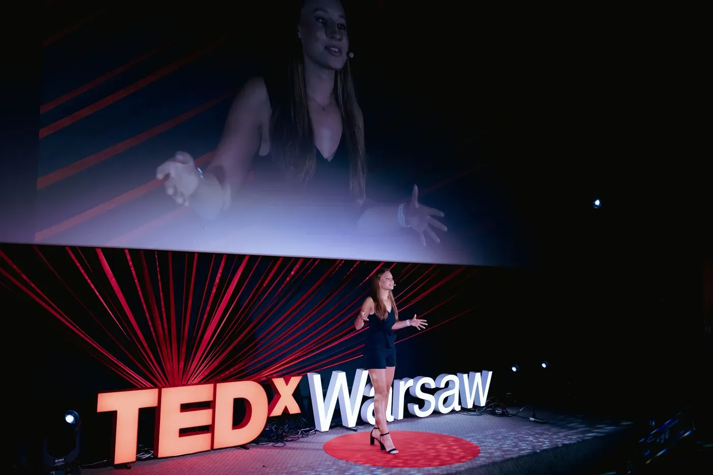 Zofia Kierner speaking on the TEDxWarsaw stage, her talk projected on the screen behind her